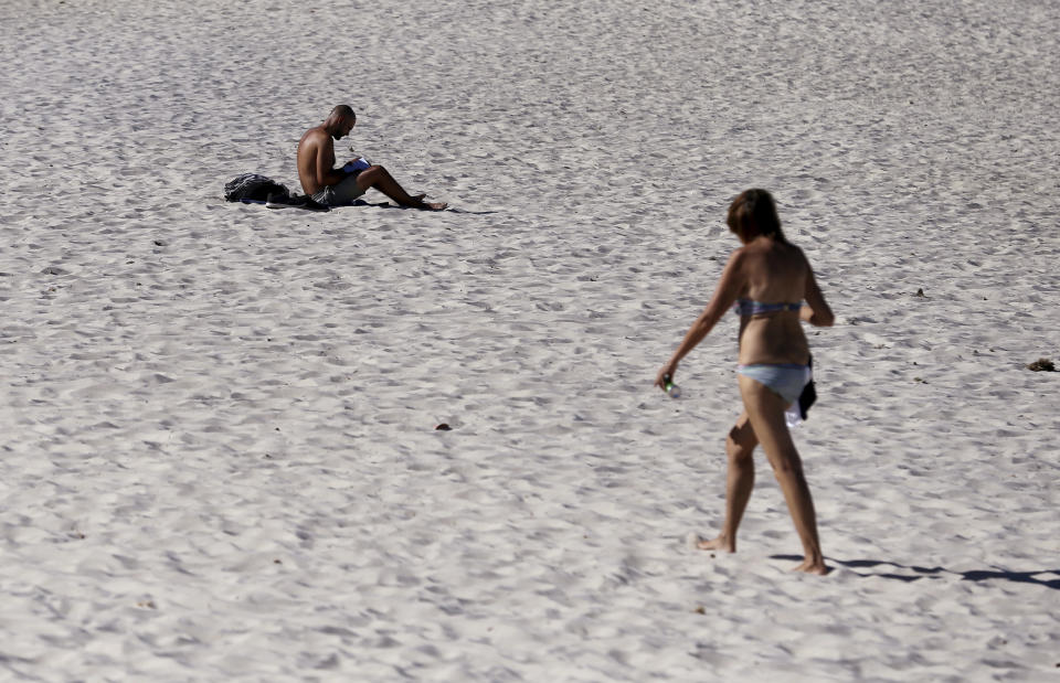 In this Jan. 24, 2019, photo, a man and a woman are on Glenelg Beach in Adelaide, Australia, as temperatures climb to 45 Celsius (113 ‎Fahrenheit). Australia has sweltered through its hottest month on record in January and the summer of extremes continues with wildfires razing the drought-parched south while expanses of the tropical north are flooded. (Kelly Barnes/AAP Image via AP)