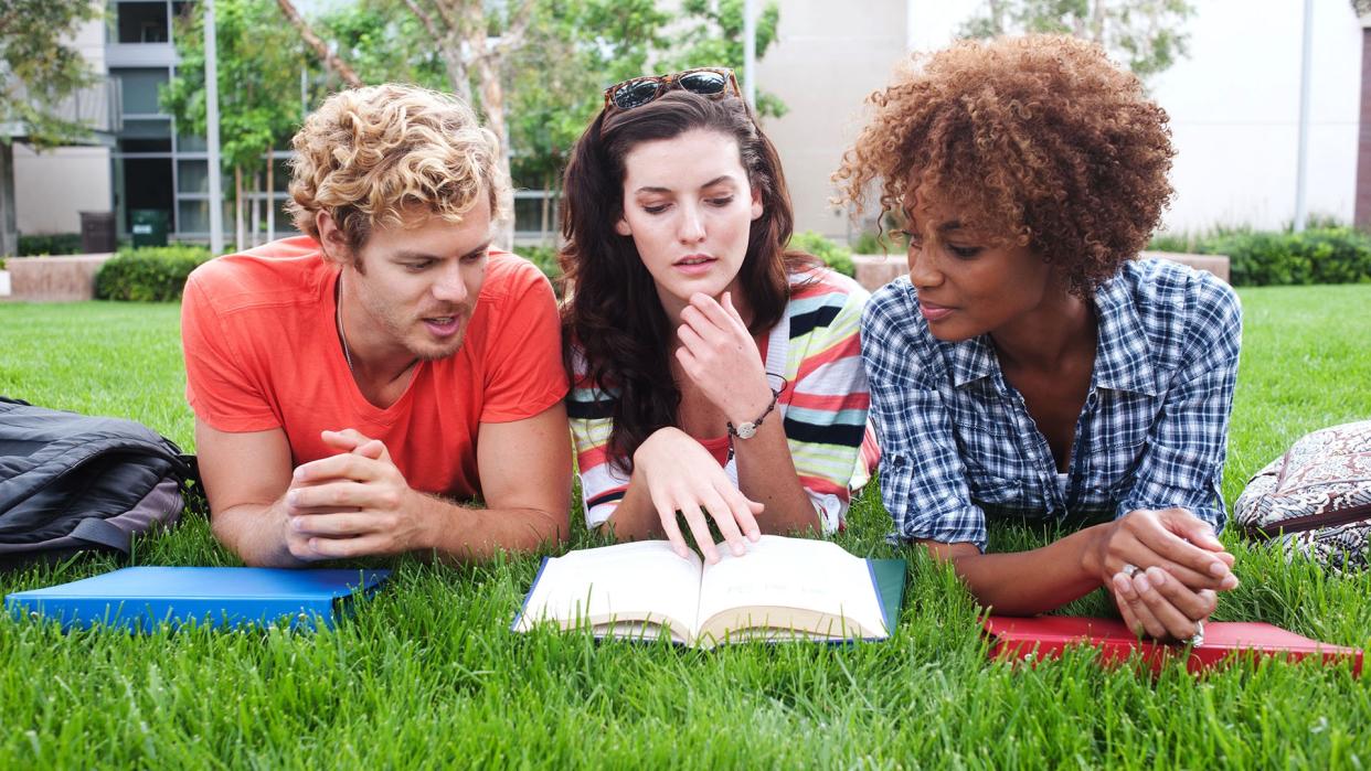 three friends laying on the grass reading a book