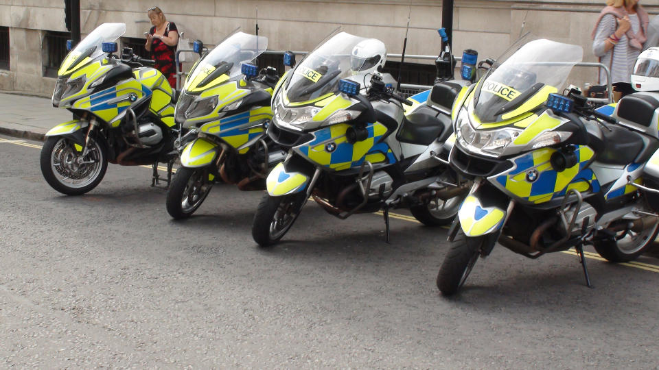 View Of People Standing, Reading Text Message With Smartphone And Packed British Police Motorcycle On The Street Of Westminster London England Europe