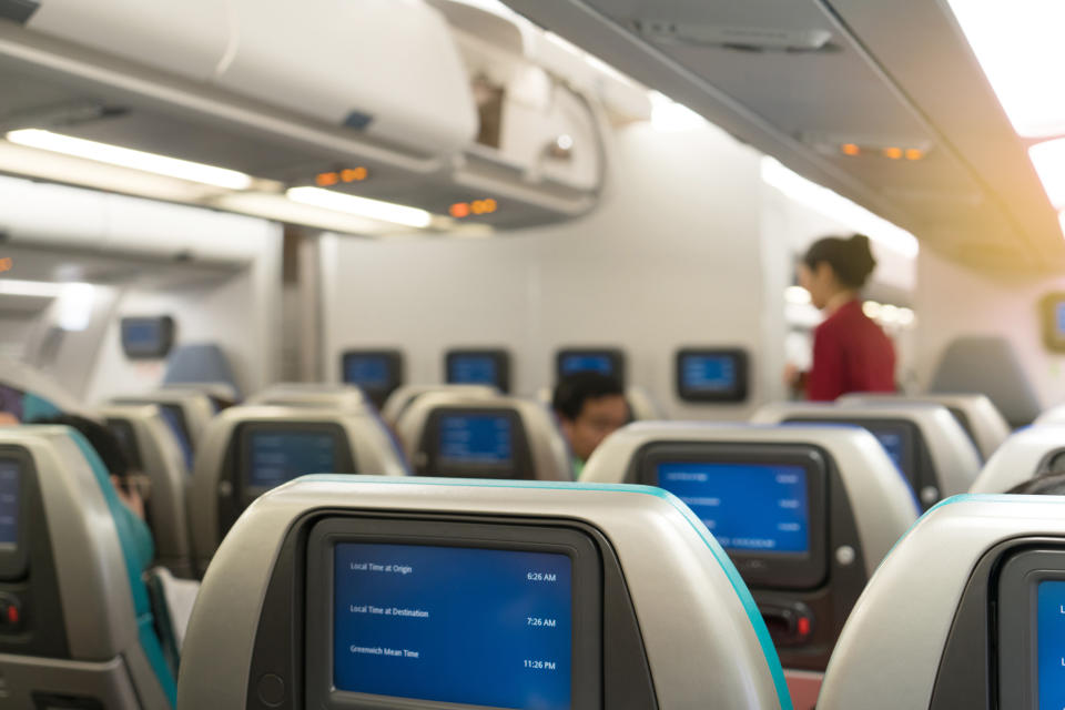 Beautiful air hostess or fight attendant waiting for service passengers on board in interior aircraft. Fight attendant with map time on monitor.