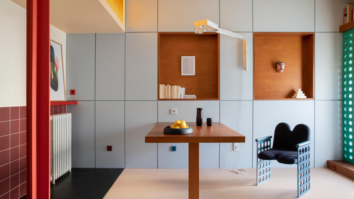  A dining area with wall-to-wall built-in cabinetry in pale blue, with a fold-down wooden table, red steel column and terracotta nooks. 