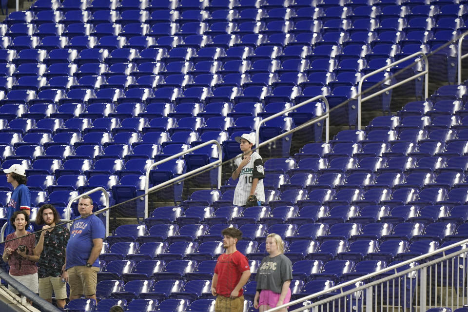 FILE - Baseball fans stand during the singing of the National Anthem before the start of a baseball game between the Miami Marlins and the Texas Rangers, Thursday, July 21, 2022, in Miami. Major League Baseball teams head into the final months of the regular season struggling to fill the stands now, even without pandemic-related attendance restrictions. (AP Photo/Wilfredo Lee, File)