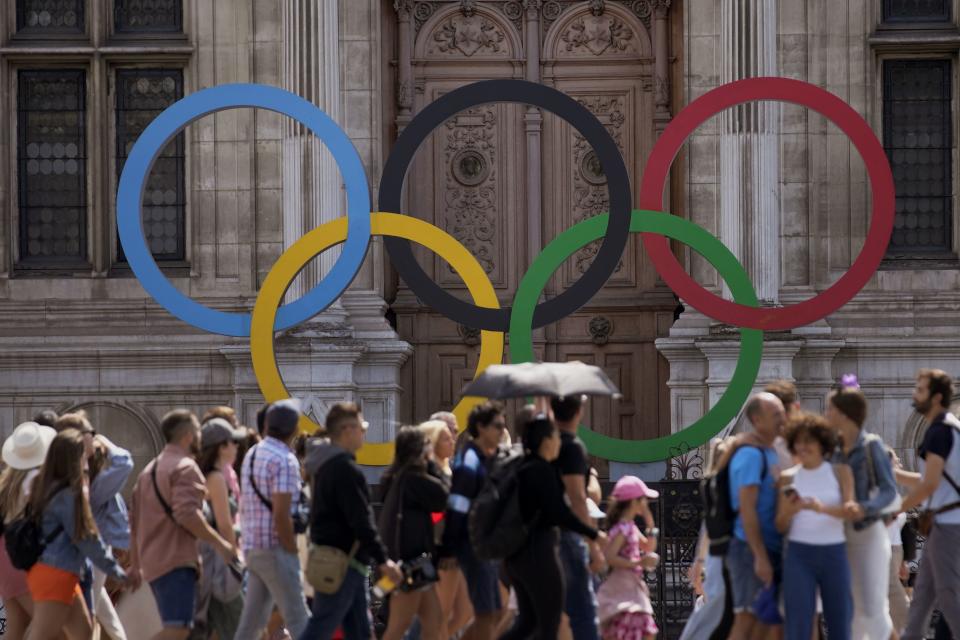 A group of tourists walk past the Olympic rings in front of the Paris City Hall with one year to until the Paris 2024 Olympic Games opening ceremony, Wednesday, July 26, 2023. | Christophe Ena, Associated Pres