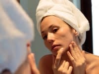 A woman looking into a mirror and holding her face while examining her acne scarring.