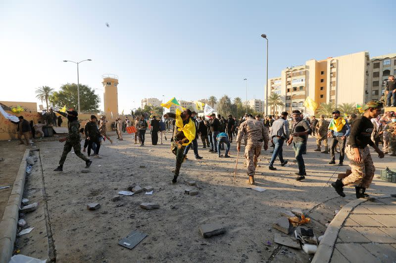 Protesters and militia fighters throw stones towards the U.S. Embassy during a protest to condemn air strikes on bases belonging to Hashd al-Shaabi (paramilitary forces), in Baghdad