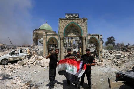 Members of the Counter Terrorism Service pose for a picture with an Iraqi flag in front of the ruins of Grand al-Nuri Mosque at the Old City in Mosul, Iraq, June 30, 2017. REUTERS/Alaa Al-Marjani