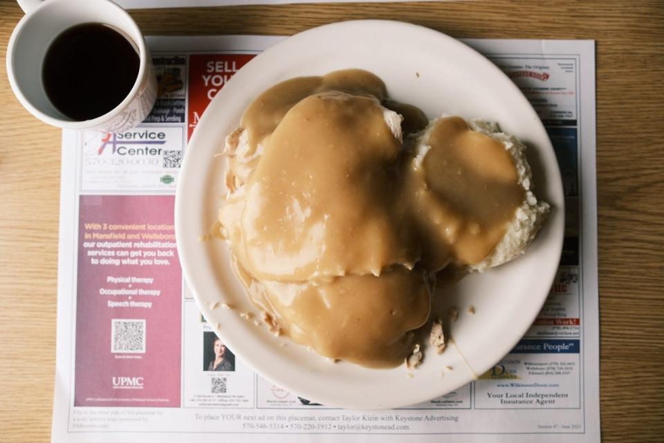 Plate covered in gravy on a placemat next to a cup of coffee