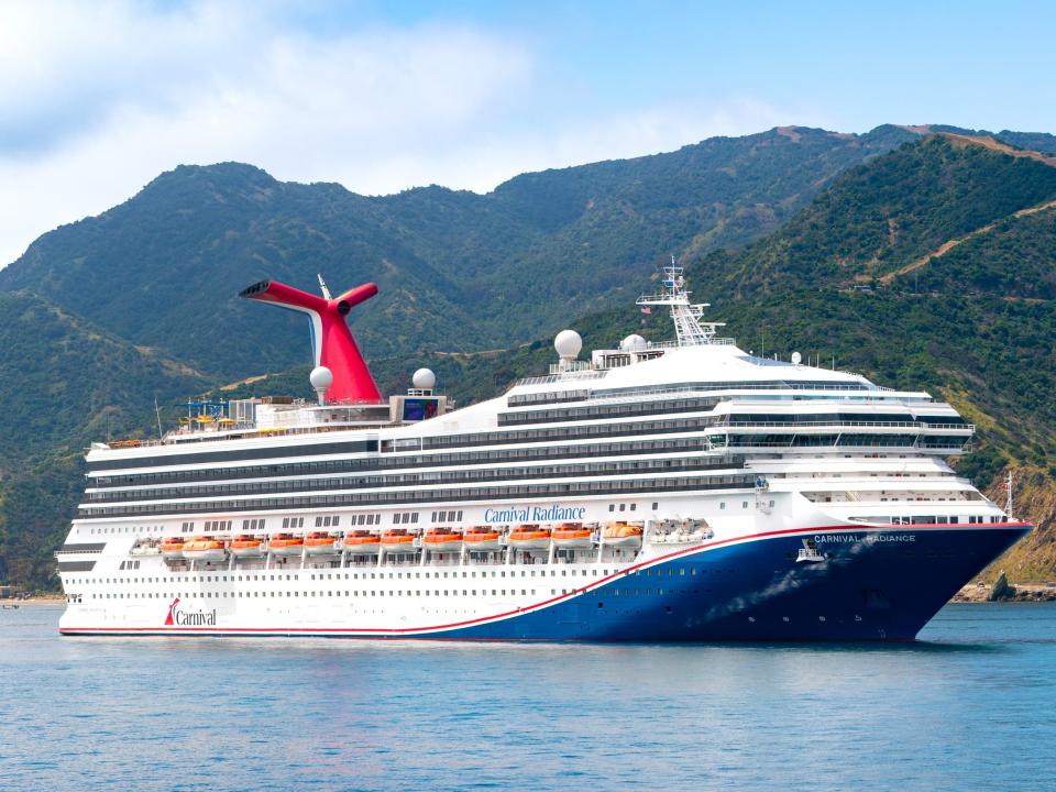 General views of the Carnival Radiance cruise ship at Avalon harbor with mountains and cloudy, blue skies in the background.