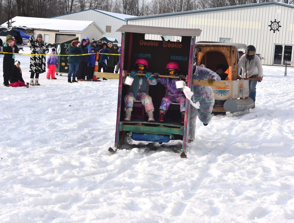 The outhouse team named "Double Dootie" takes the lead in a race Saturday, Feb. 4, 2023, against the Manitou Beach Marina team during the Devils Lake Tip-Up Festival. The Saturday afternoon outhouse races were held on land at Manitou Beach Marina rather than on the ice due to safety concerns with the thickness of the ice. Riding in "Double Dootie" are Charlotte Ender, 8, and Arrabella Ender, 6.