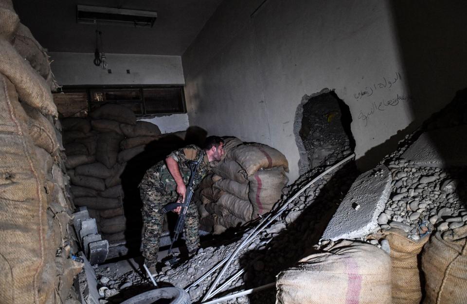 A photo of a solider looking inside of a hole in the wall that leads to a larger tunnel under the municipal stadium in Raqa