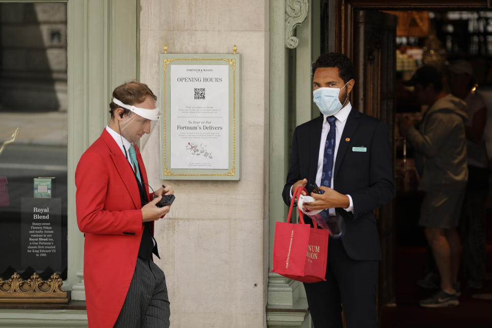 A doorman wearing a face shield to protect from coronavirus stands with a colleague at the main entrance of the Fortnum & Mason department store in the Piccadilly area of central London, Friday, May 22, 2020. The store reopened its food hall department for customers to enter yesterday as part of a phased reopening as the British government is beginning to relax aspects of its nationwide coronavirus lockdown. (AP Photo/Matt Dunham)