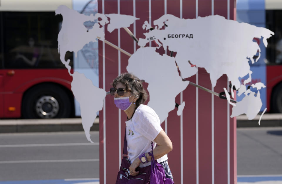 A woman wearing a mask against the spread of the coronavirus passes a billboard shows a world map in Belgrade, Serbia, Monday, Aug. 23, 2021. (AP Photo/Darko Vojinovic)