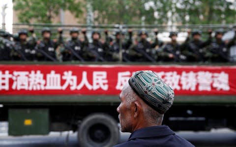 A Uighur man looks on as a truck carrying paramilitary policemen travel along a street during an anti-terrorism oath-taking rally - Credit: REUTERS/Stringer/File Photo&nbsp;