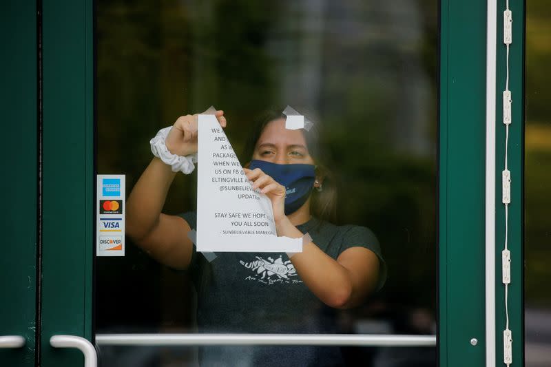 Una mujer retira un anuncio sobre el cierre de la tienda Sunbelievable por motivos de salud, antes de que reabra en contra de las recomendaciones de salud locales, mientras el brote de la enfermedad coronavirus (COVID-19) continúa en el distrito de Staten Island de Nueva York.