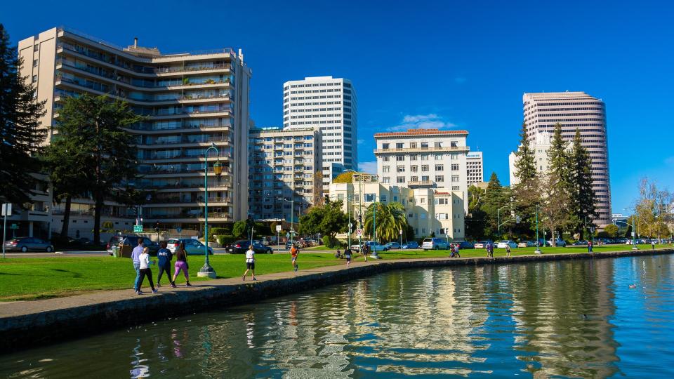 Women and men walking and jogging along the Downtown Oakland waterfront with Lake Merritt in the foreground.