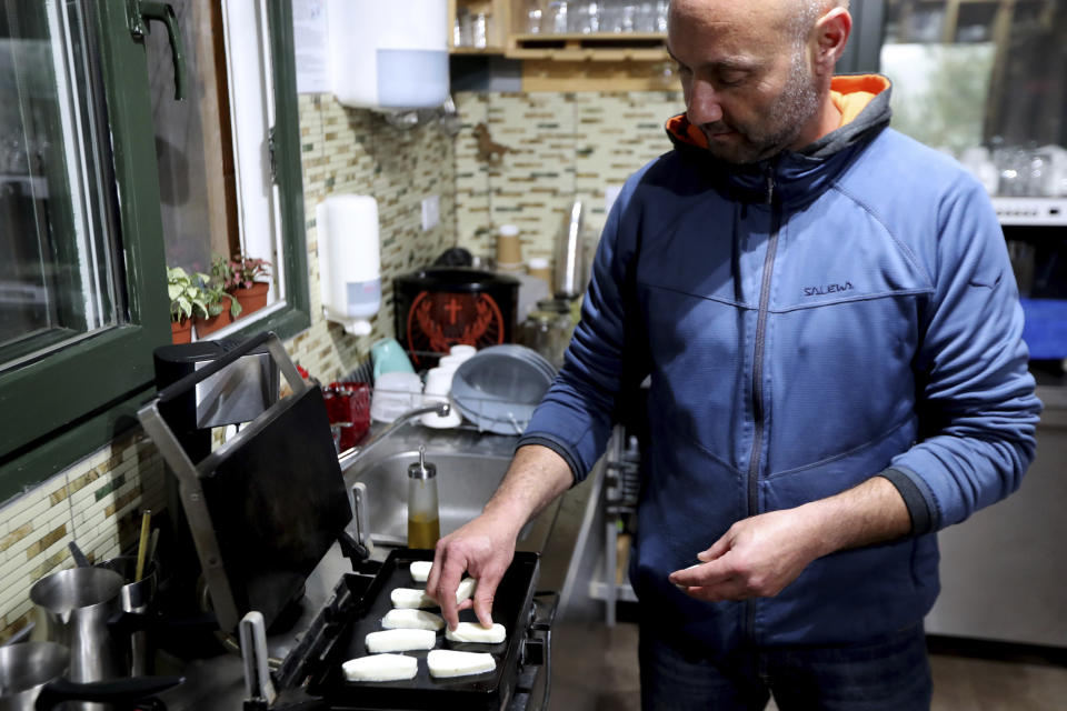 In this photo taken Wednesday Dec. 11, 2019, Cypriot farmer Vasilis Kyprianou, 48, roasts Cyprus' halloumi cheese at his farm in Kampia village near Nicosia, Cyprus. Cyprus' halloumi cheese, with a tradition dating back some five centuries, is the island nation's leading export. It's goat and sheep milk content makes it a hit with health-conscious cheese lovers in Europe and beyond. It's added appeal is that unlike other cheeses, it doesn't melt when heated up. (AP Photo/Petros Karadjias)