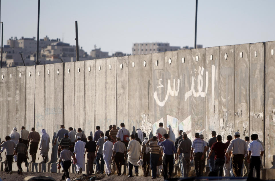 FILE - In this Friday, Aug. 10, 2012, file photo, Palestinian men pass near a section of Israel's separation barrier on their way to pray at the Al-Aqsa Mosque in Jerusalem, on the fourth Friday of the Muslim holy month of Ramadan near the West Bank city of Ramallah. John Kerry’s warning that Israel could become an “apartheid state” if it doesn’t reach a peace deal with the Palestinians has set off an uproar in Israel and angered Israel’s allies in Washington. Kerry was forced to backtrack from his comments, but he voiced an opinion that is frequently heard in Israel itself and tapped into a debate that has become increasingly heated in recent years. (AP Photo/Majdi Mohammed, File)