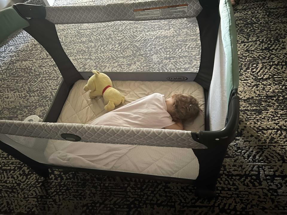 A baby napping in her crib with a stuffed animal next to her.