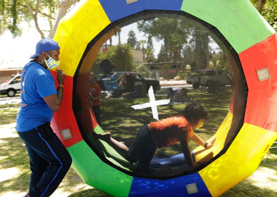 man in a mask helps a kid roll in an inflatable trampoline during COVID-19 pandemic