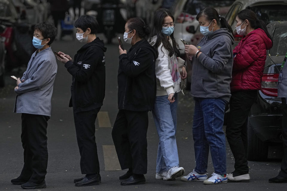 A woman wearing a face mask to help curb the spread of the coronavirus walks through a line of masked service sector women waiting to receive a swab for the COVID-19 test during a mass testing in Beijing, Friday, Oct. 29, 2021, following a spike of the coronavirus in the capital and other provincials. (AP Photo/Andy Wong)
