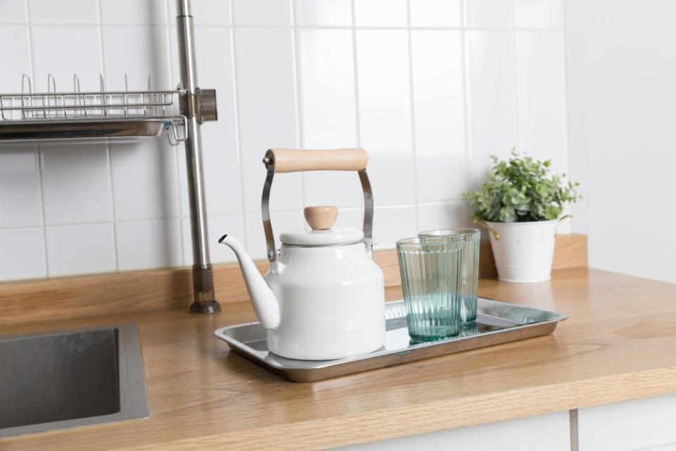 Kettle on wooden counter in front of vertically-stacked white backsplash tiles in kitchen