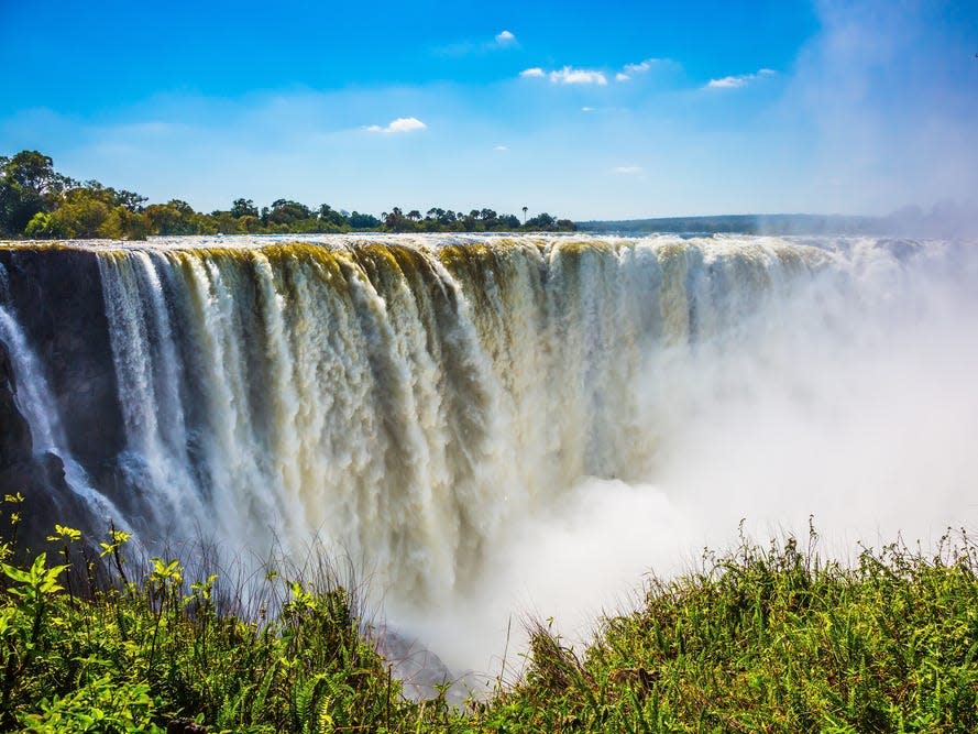 A large waterfall on a sunny day. There is grass in the foreground.