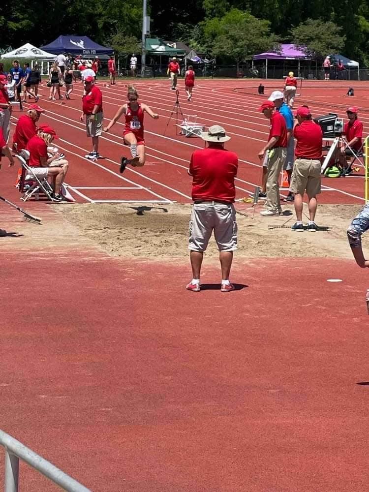 BNL's Tori Longsdon launches off the long jump board under the watchful eye of coach Mike Branam (in bucket hat) at Saturday's Unified Track & Field State Finals.
