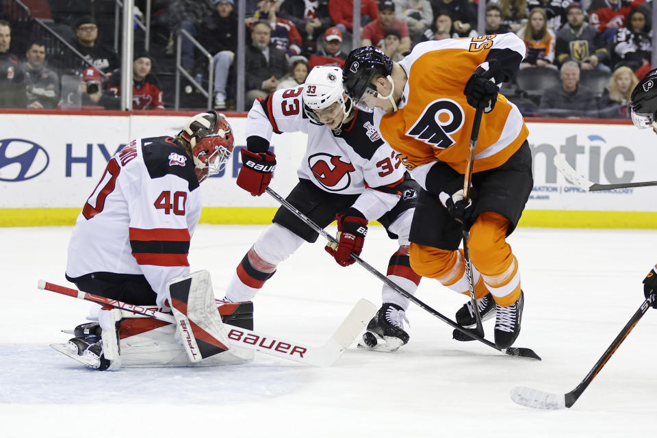 New Jersey Devils goaltender Akira Schmid, left, defends as Devils' Ryan Graves (33) battles for the puck with Philadelphia Flyers defenseman Rasmus Ristolainen, right, during the first period of an NHL hockey game Saturday, Feb. 25, 2023, in Newark, N.J. (AP Photo/Adam Hunger)
