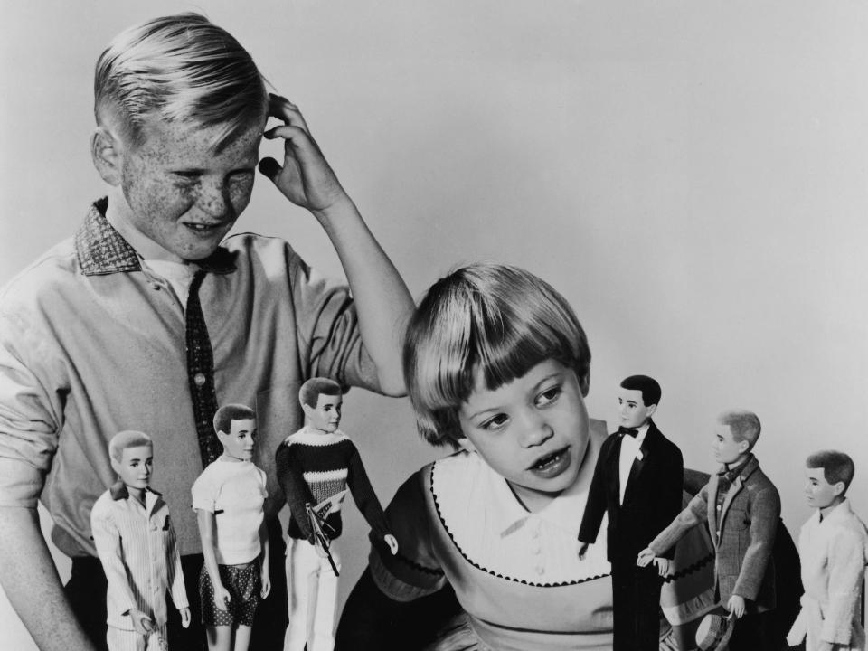 A young boy looks confused while a young girl inspects Ken dolls in 1961.