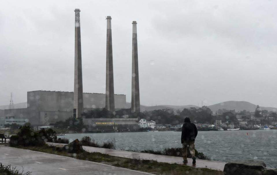 A person takes a rain-soaked walk in Morro Bay last January, with the closed Duke Energy power plant in the background.