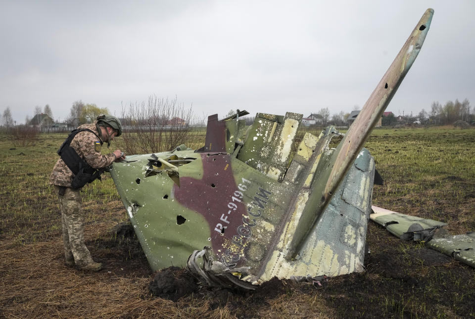 A Ukrainian soldier examines a fragment of a Russian Air Force Su-25 jet after a recent battle at the village of Kolonshchyna, Ukraine, Thursday, April 21, 2022.(AP Photo/Efrem Lukatsky)