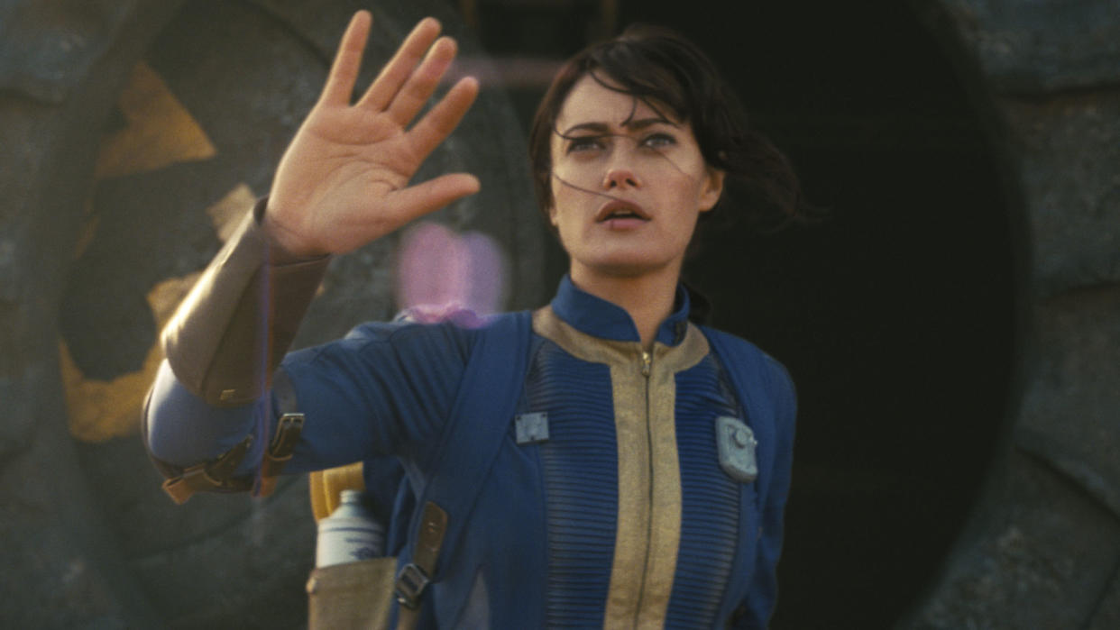  Lucy emerges from Vault 33 with her right hand raised in Amazon's Fallout TV show. 