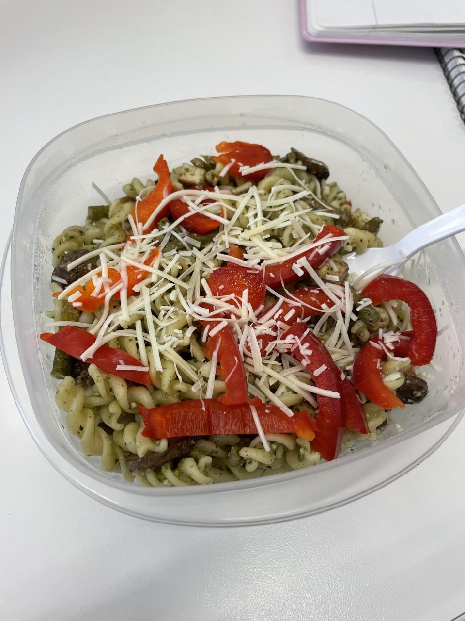 A plastic container with pasta, peppers, and shredded cheese, ready for a meal