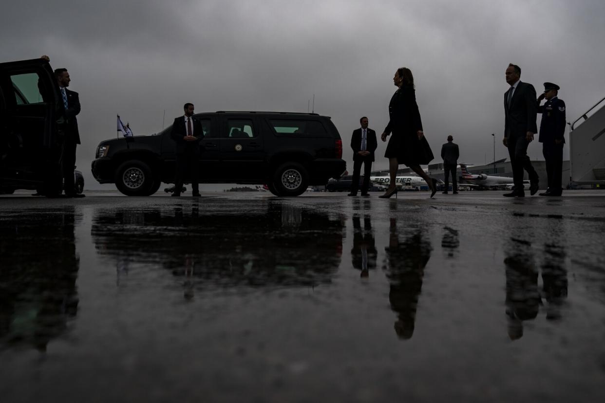 Kamala Harris walks outside under cloudy skies with water on the pavement