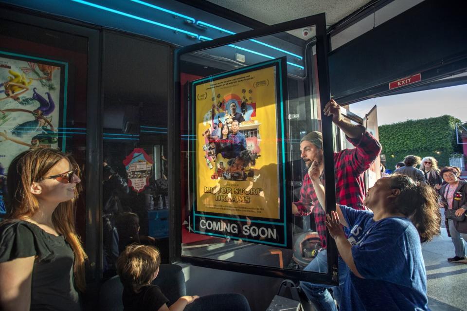 Surrounded by other people, a man places a movie poster inside a display case at a cinema exterior.