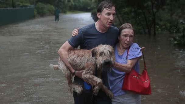 PHOTO: Andrew White (L) helps a neighbor down a street after rescuing her from her home in his boat in the upscale River Oaks neighborhood after it was inundated with flooding from Hurricane Harvey, Aug. 27, 2017, in Houston. (Scott Olson/Getty Images)