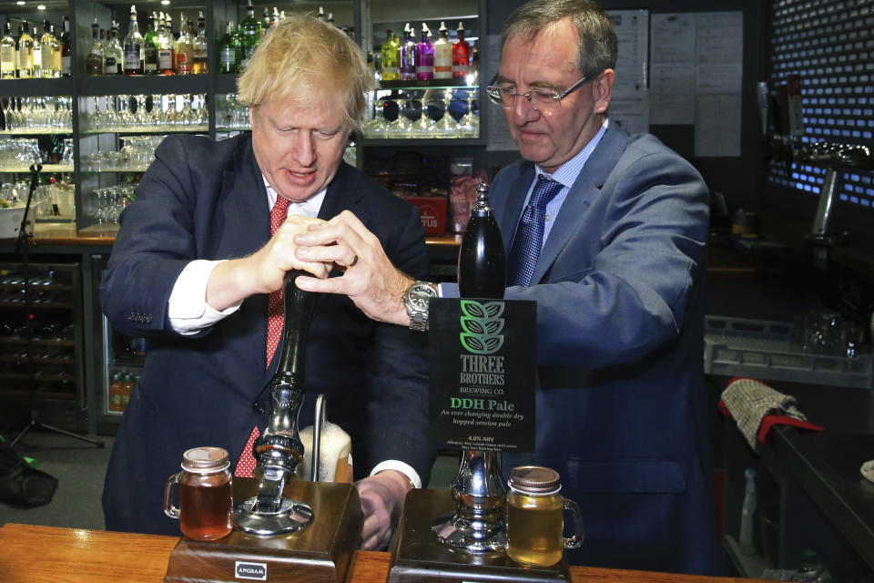 Britain's Prime Minister Boris Johnson pulls a pint with newly elected Conservative party MP for Sedgefield, Paul Howell at Sedgefield Cricket Club in County Durham, north east England, Saturday Dec. 14, 2019, following his Conservative party's general election victory. Johnson called on Britons to put years of bitter divisions over the country's EU membership behind them as he vowed to use his resounding election victory to finally deliver Brexit. (Lindsey Parnaby/Pool via AP)