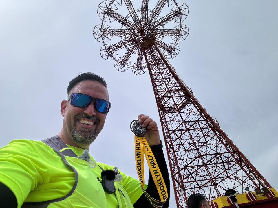 A man shows off his Brooklyn half-marathon medal in front of the famed Coney Island Tower in New York.