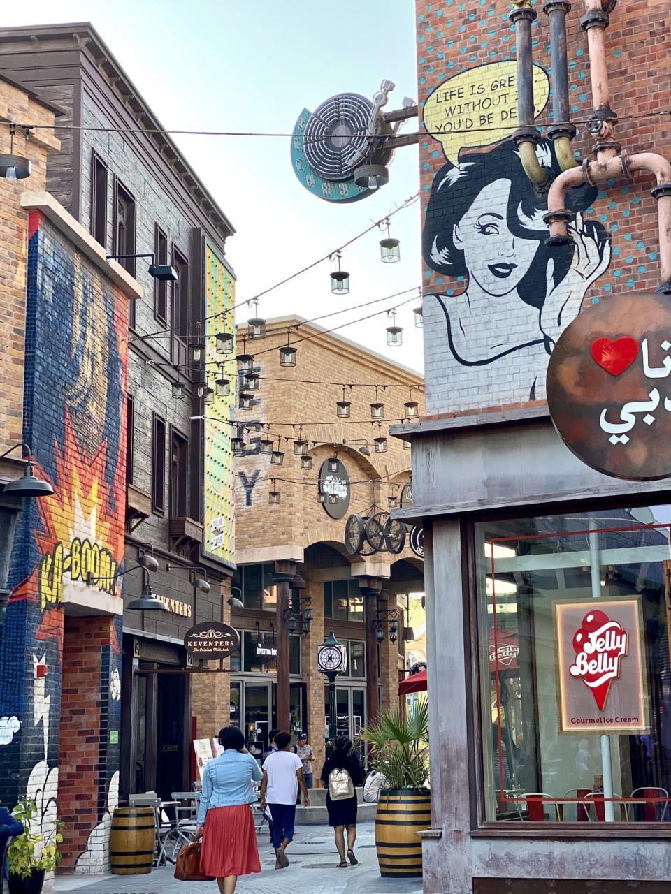 exterior shot of street art and murals of La Mer in Dubai, shoppers walking down path between buildings