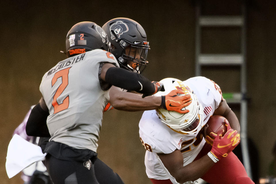 Oklahoma State safety Tanner McCalister, left, and Oklahoma State cornerback Christian Holmes, center, reaches for the head of Iowa State running back Breece Hall (28) during the second half of an NCAA college football game Saturday, Oct. 24, 2020, in Stillwater, Okla. AP Photo/Brody Schmidt)