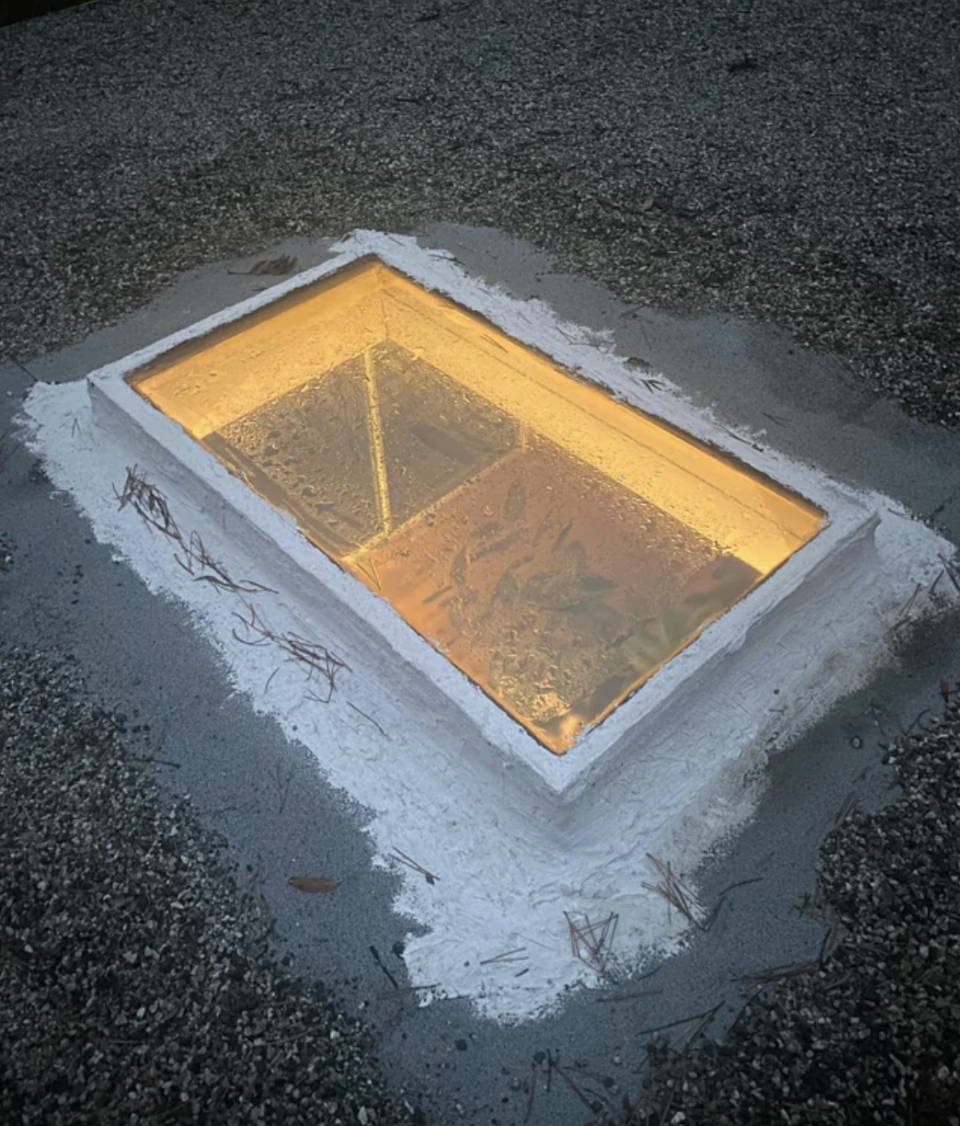 A lit-up empty pool at dusk with a house's reflection