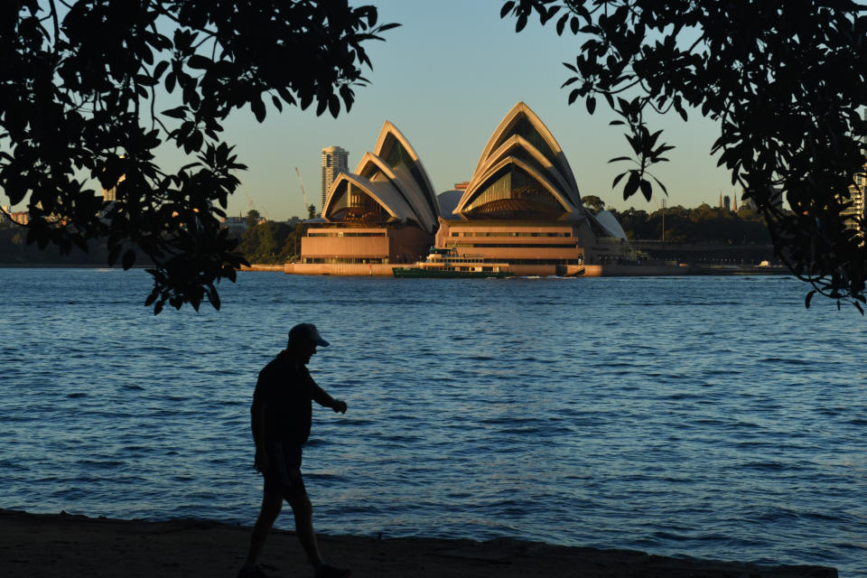 A man walks along the harbour opposite the Sydney Opera House.