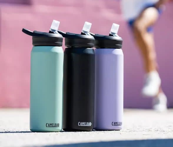 Two blurred runners in activewear are in the background, with three CamelBak water bottles in the foreground. Featured in a shopping article