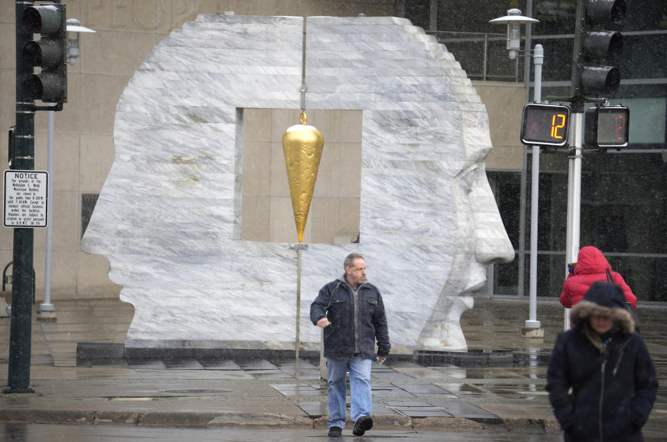 A pedestrian crosses Colfax Avenue in front of the Larry Kirkland sculpture called East 2 West Source Point outside the south entry of the Wellington Webb Building as a light snow from a spring storm swept over the intermountain West Tuesday, April 4, 2023, in Denver. Forecasters predict that the storm will move out of the region on Tuesday and over the northern plains states where some locations could see up to two feet of snow. (AP Photo/David Zalubowski)