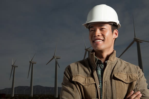 A man wearing a hard hat with wind turbines in the background