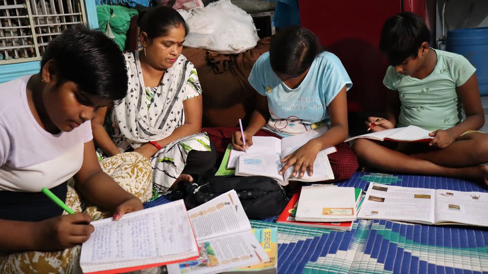 Savita helps her children with homework at a temporary home in Delhi. - Rhea Mogul/CNN