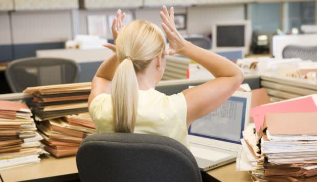 Businesswoman in cubicle with laptop and stacks of files