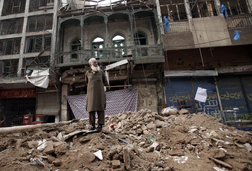 A man stands on a pile of rubble in front of a damaged building after it was hit by a bomb blast, which happened on Sunday, in Peshawar