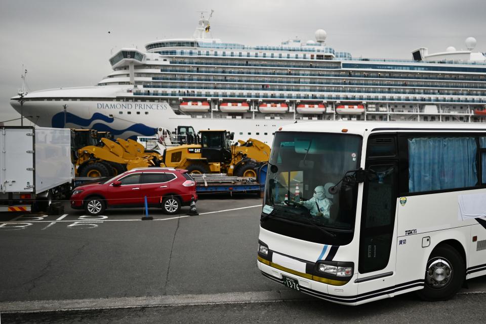 A bus with a driver wearing full protective gear departs from the dockside next to the Diamond Princess cruise ship.