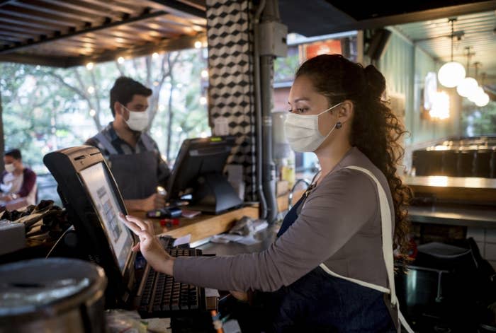 A masked server at a restaurant enters a customer's order into the POS system